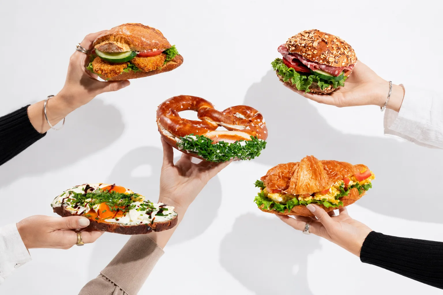 F&uuml;nf H&auml;nde halten belegte Br&ouml;tchen, Brezel, Stulle und Croissant von Huck